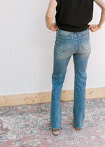 Back view of model wearing a black top with high waisted jeans a faded wash, bootcut and a raw hem.