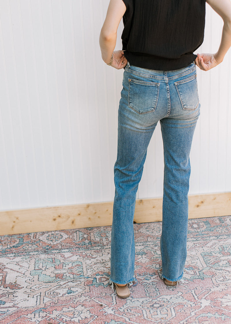 Back view of model wearing a black top with high waisted jeans with a faded wash, bootcut and a raw hem.