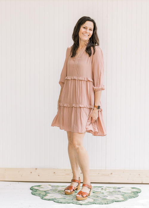 Model wearing a blush above the knee dress with 3/4 bubble sleeves, v-neck and tiers with ruffles. 