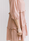 Close up of 3/4 bubble sleeves and tiers with ruffles on a model in an above the knee blush dress. 