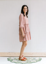 Side view of Model wearing a blush above the knee dress with 3/4 bubble sleeves, v-neck and tiers. 