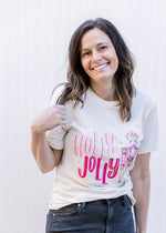 Model wearing a cream short sleeve tee with a round neck, holly jolly in pink and a nutcracker. 