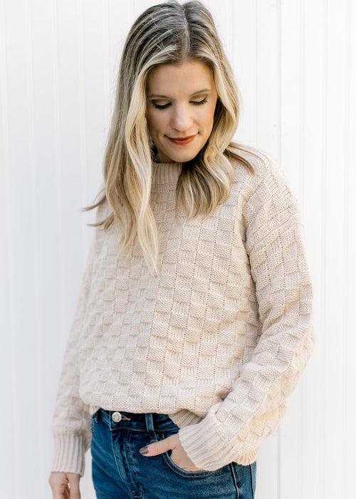 Model wearing a tan textured sweater with checkered knit, long sleeves and a round neck. 