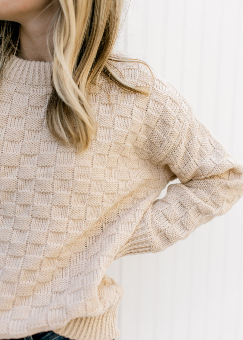 Close up of checkered knit pattern on a tan sweater with long sleeves and an acrylic material.