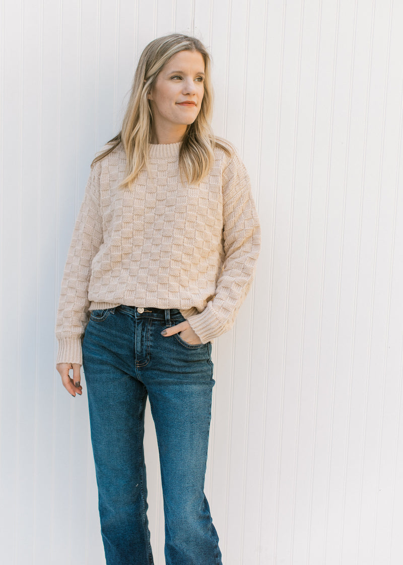 Model wearing jeans with a tan textured sweater with checkered knit, long sleeves and a round neck. 
