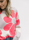 Close up of coral flowers with a light purple center on a cream sweater with long sleeves. 