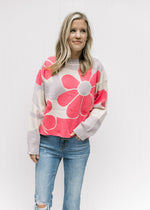 Model wearing jeans and a cream sweater with coral flowers and a slightly cropped fit.