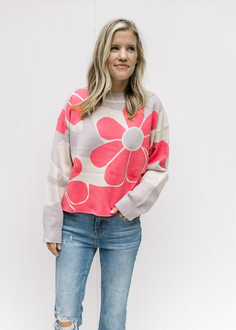 Model wearing jeans and a cream sweater with coral flowers and a slightly cropped fit.