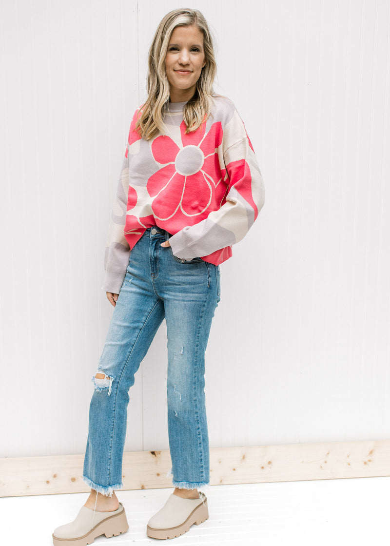 Model wearing jeans, mules and a cream sweater with coral flowers and long sleeves.