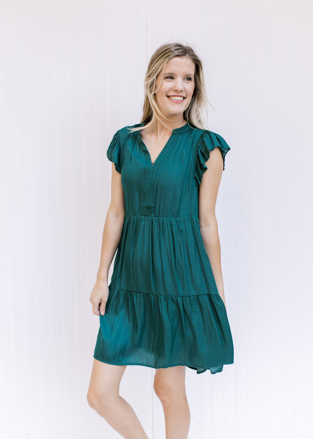 Model wearing a hunter green above the knee dress with a v-neck and a ruffle cap sleeve. 