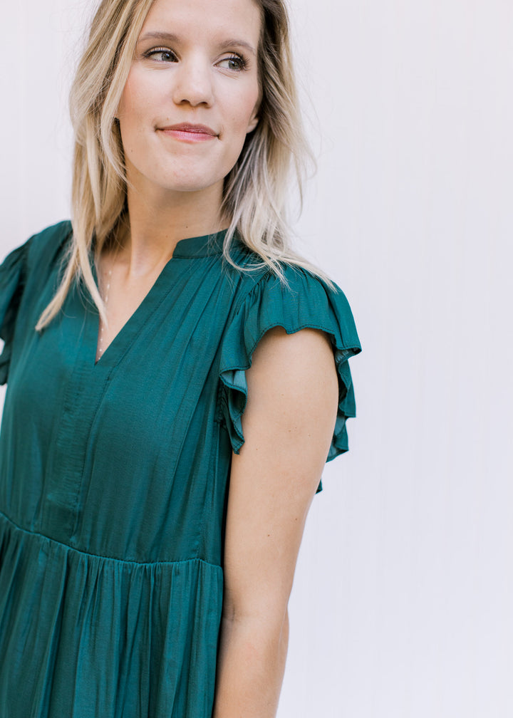 Close up of ruffle cap sleeve and v-neck on a hunter green above the knee, lightweight dress. 