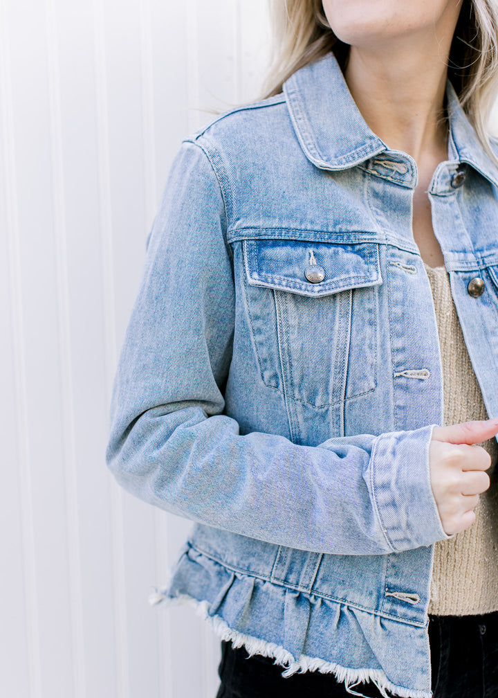 Model wearing a light denim jacket with a button closure, ruffled raw hem and long sleeves. 