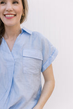 Close up of v-neck, patch pockets and rolled short sleeves on a pale blue top.