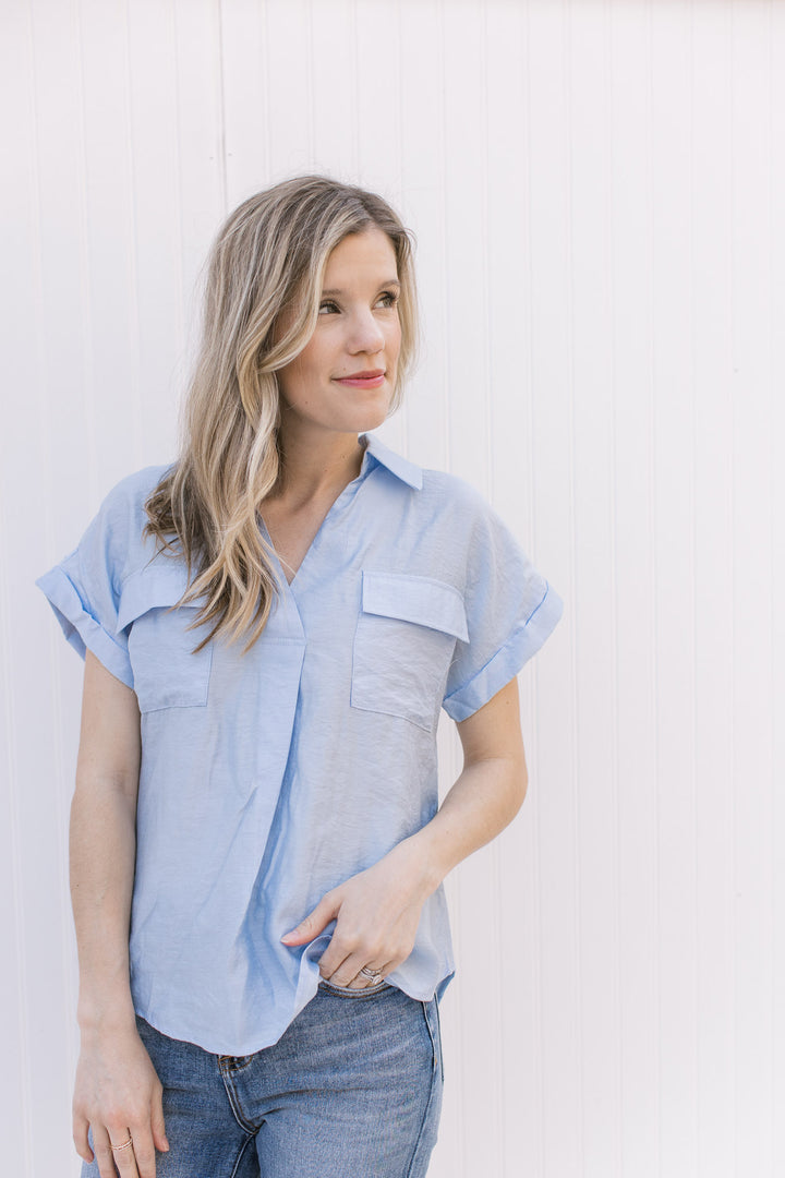 Model wearing a pale blue top with patch pockets, v-neck, collar and rolled short sleeves. 