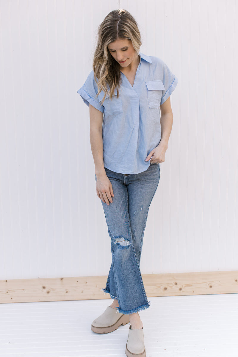 Model wearing jeans, mules anD a pale blue top with patch pockets and rolled short sleeves.