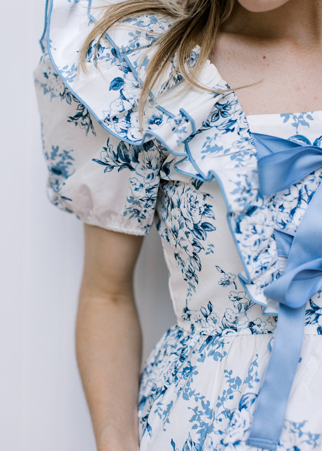 Model wearing a white short sleeve top with blue floral, square neck and double front bow ties.
