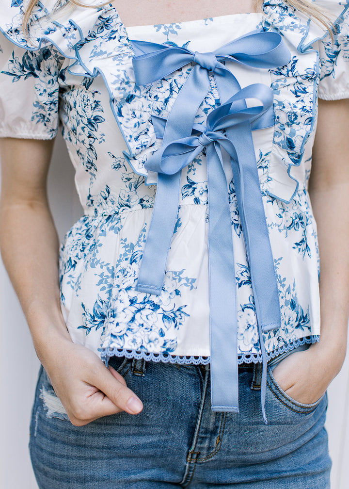 Model wearing a white short sleeve top with blue time and floral, and double front bow ties.