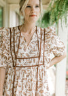 Close up of ruffle at shoulder, and short puff sleeves on a cream dress with flowers. 