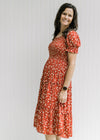 Model wearing a maroon midi dress with a cream floral pattern, smocked bodice and a tiered skirt.