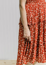 Close up of the tiers on the skirt portion on a maroon midi dress with a cream floral pattern. 
