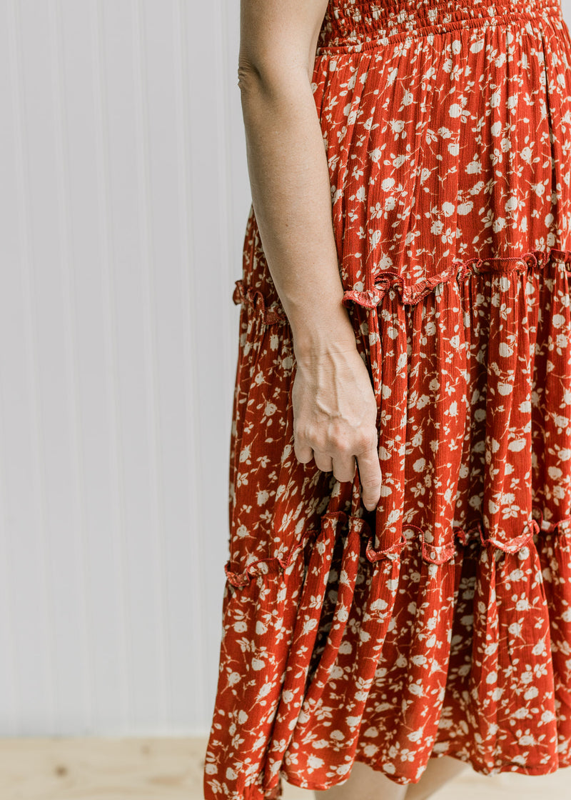 Close up of the tiers on the skirt portion on a maroon midi dress with a cream floral pattern. 