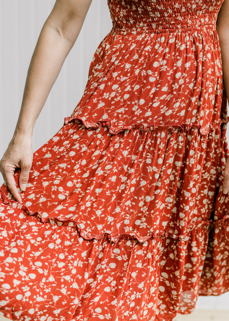 Close up of model holding out a maroon midi dress with tiers and a cream floral pattern. 