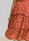 Close up view of tiering on the skirt of a maroon midi dress with a cream floral pattern. 