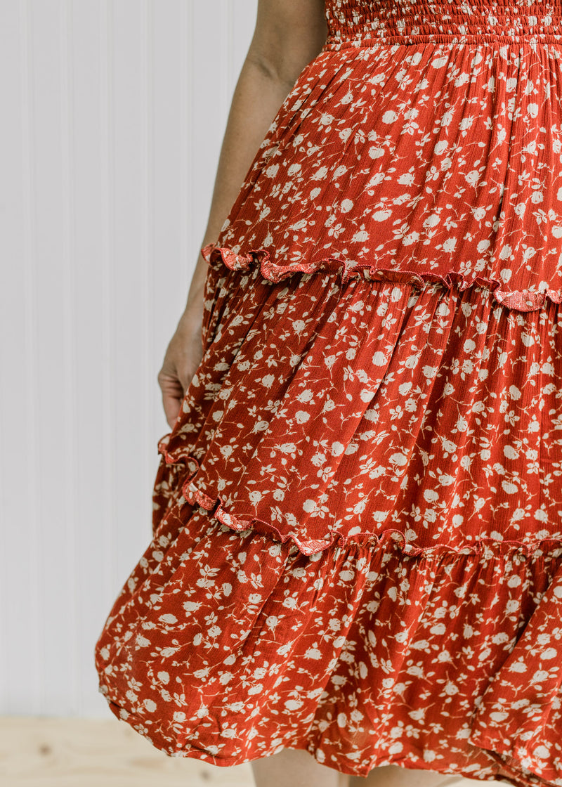 Close up view of tiering on the skirt of a maroon midi dress with a cream floral pattern. 