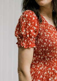 Close up of smocked bodice and short bubble sleeve on a maroon dress with a cream floral pattern. 