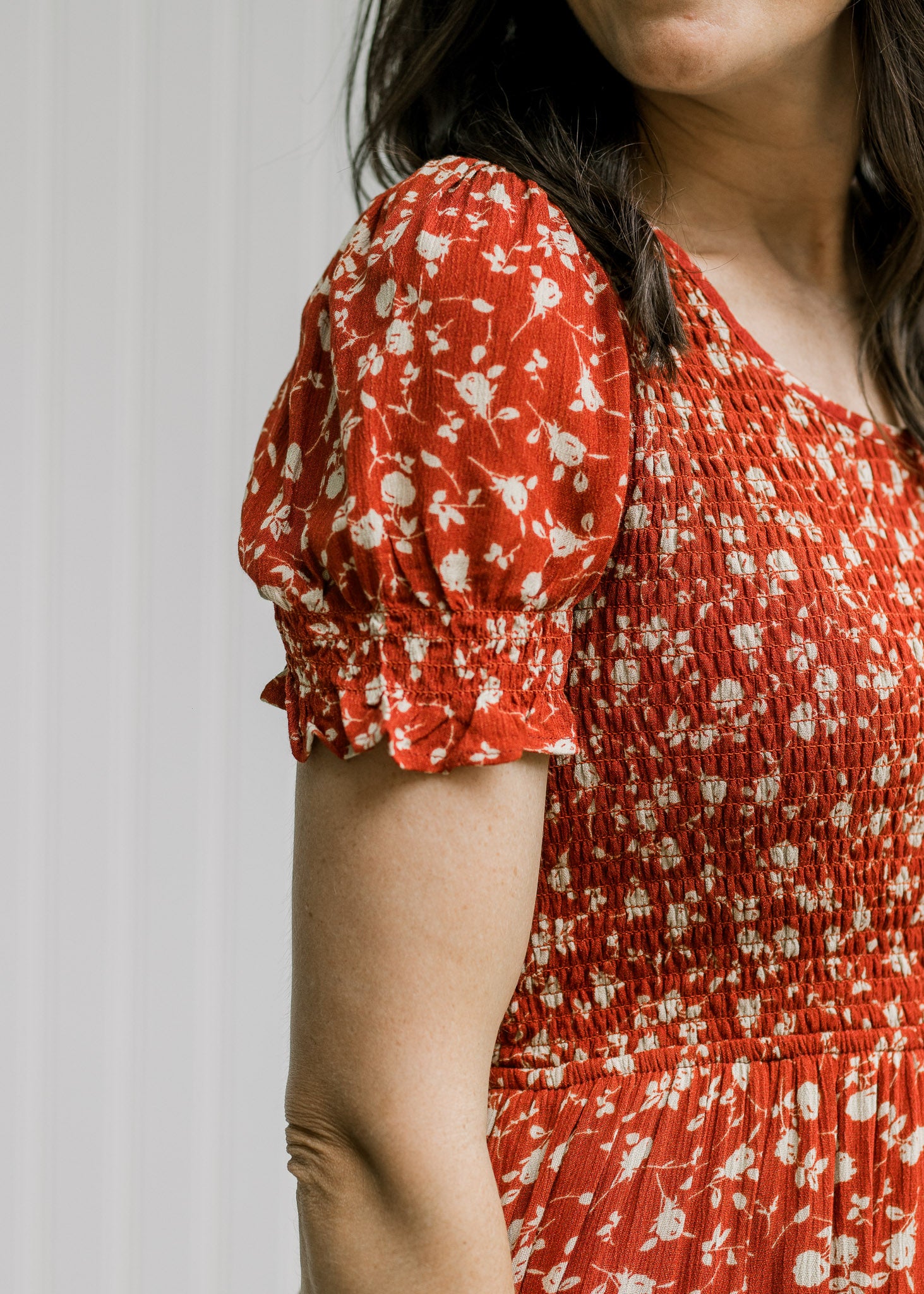Close up of smocked bodice and short bubble sleeve on a maroon dress with a cream floral pattern. 