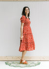 Model wearing sandals with a maroon midi with a cream floral pattern and bubble short sleeves.