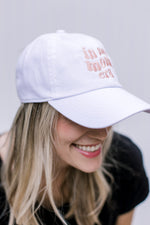 Side view of Model wearing an white size hat with pink embroidered script “in my mom era”.