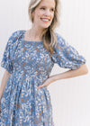 Close up of smocked bodice and bubble short sleeves on a dusty blue dress with a floral Pattern.