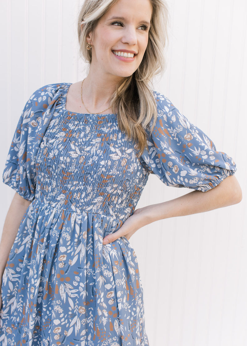 Close up of smocked bodice and bubble short sleeves on a dusty blue dress with a floral Pattern.