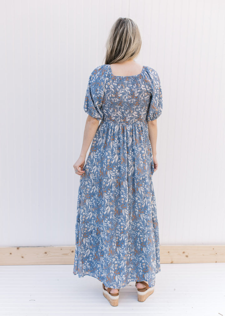 Back view of Model wearing a dusty blue dress with cream and rust floral and a smocked bodice.