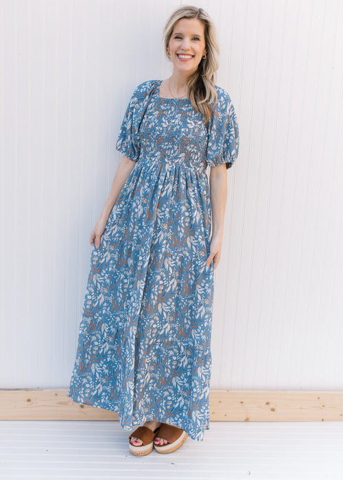Model wearing a dusty blue dress with cream and rust floral, smocked bodice and short sleeves.