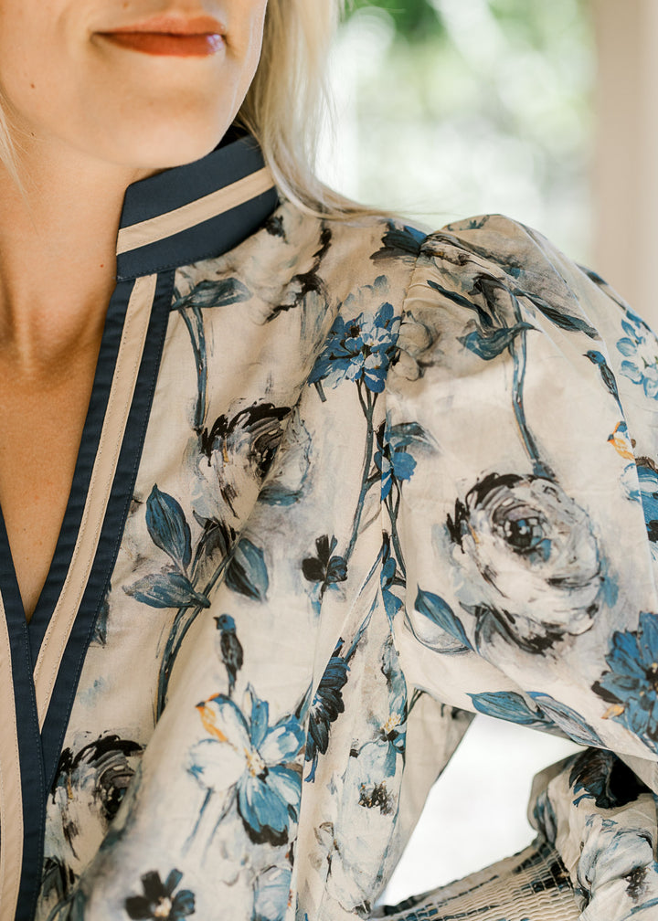Close up on navy and cream trim and v-neck on a cream blouse with blue floral pattern. 