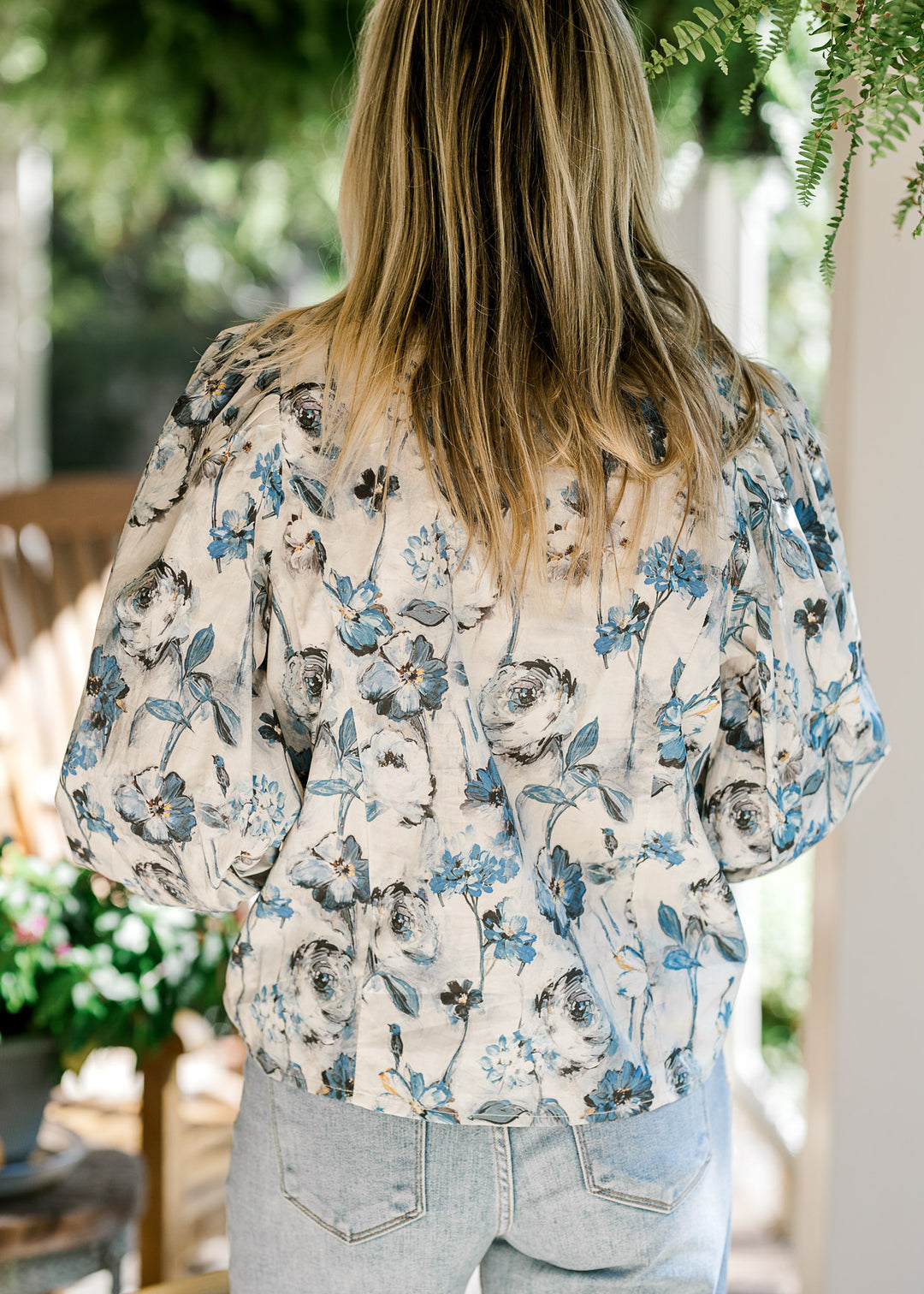 Back view of Model wearing a cream top with blue floral and long sleeves with elastic cuff. 