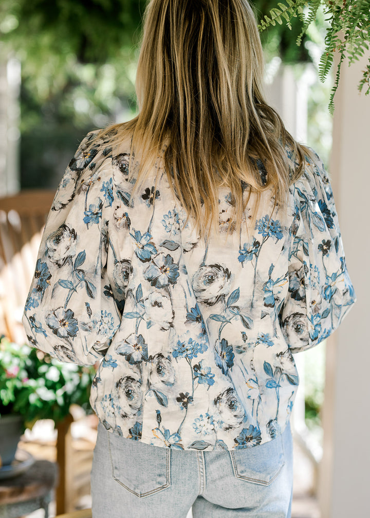 Back view of Model wearing a cream top with blue floral and long sleeves with elastic cuff. 