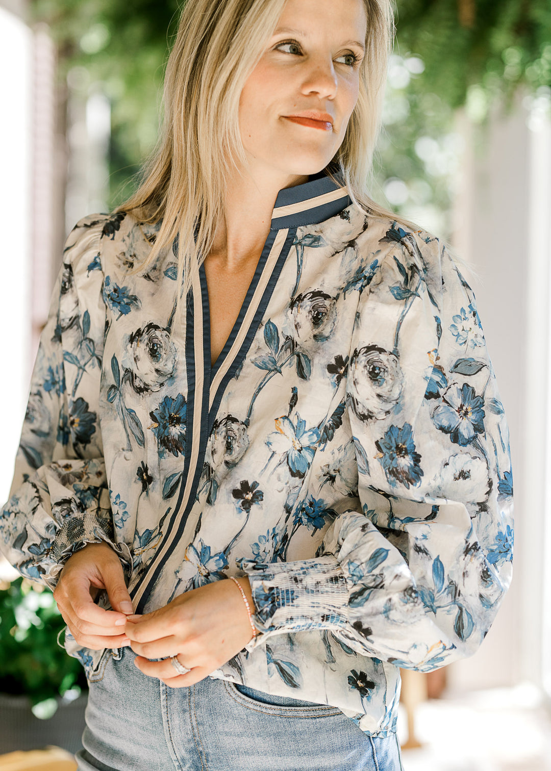 Model wearing a cream top with blue floral, navy and cream trim and long sleeves with elastic cuff. 