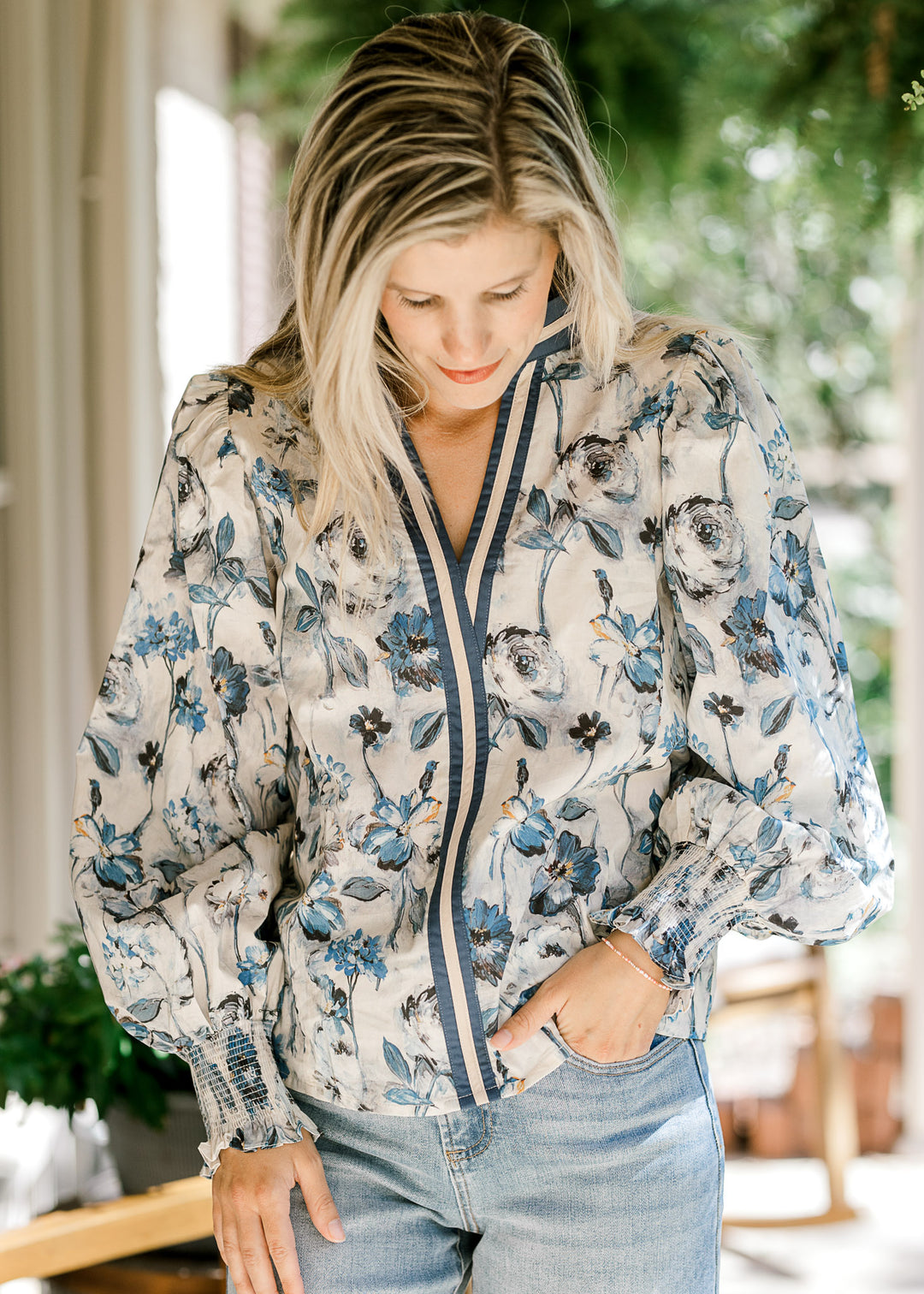 Model wearing a cream top with blue floral, navy and cream trim and long sleeves with elastic. 