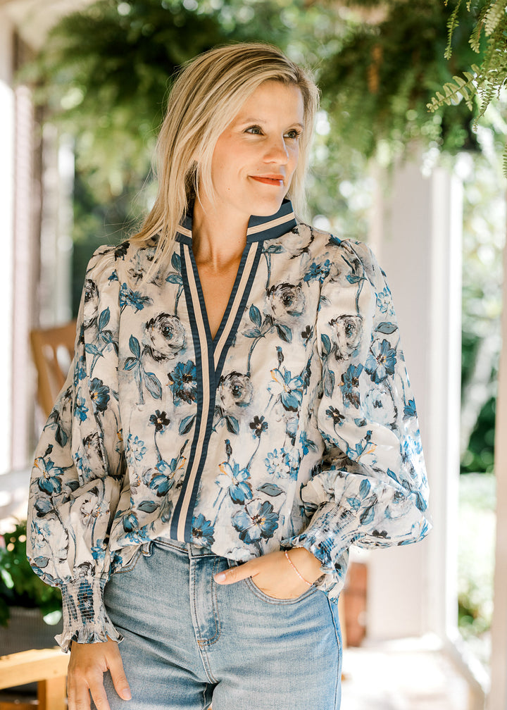 Model wearing a cream top with blue floral, navy and cream trim and bubble long sleeves. 
