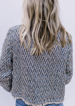 Back view of Model wearing a tweed open front jacket with a raw cropped hem and long sleeves.