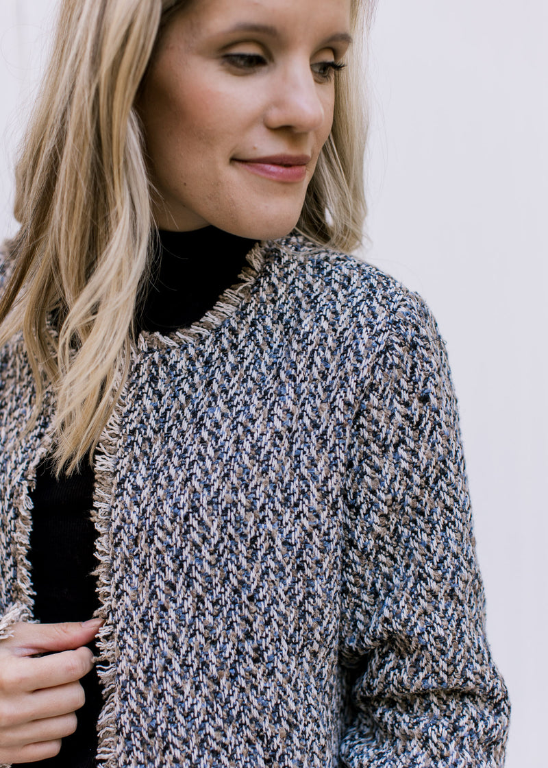 Close up of raw hemline on an open front tweed jacket with long sleeves and a slight cropped fit.