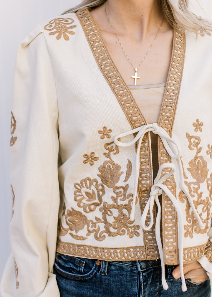 Close up of tan stitching, two tie closure and lace detail on a khaki long sleeve jacket. 