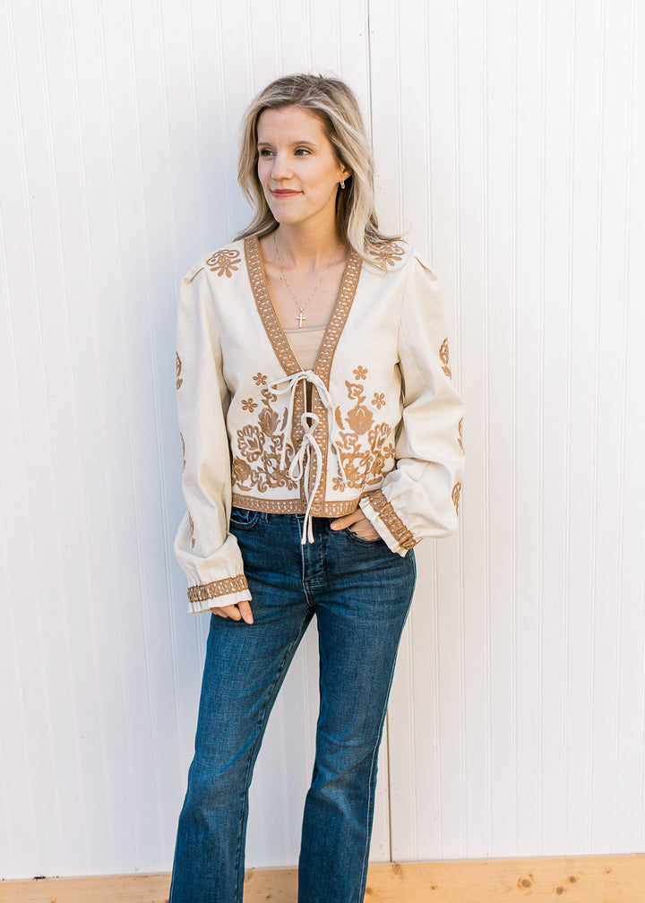 Model wearing jeans and a slightly cropped khaki jacket with tan floral and a two tie closure. 