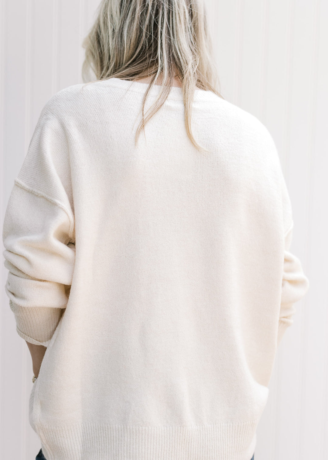 Back view of Model wearing a cream lightweight sweater with long sleeves and a round neck. 