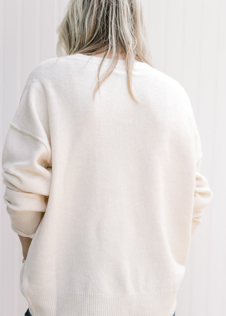 Back view of Model wearing a cream lightweight sweater with long sleeves and a round neck. 