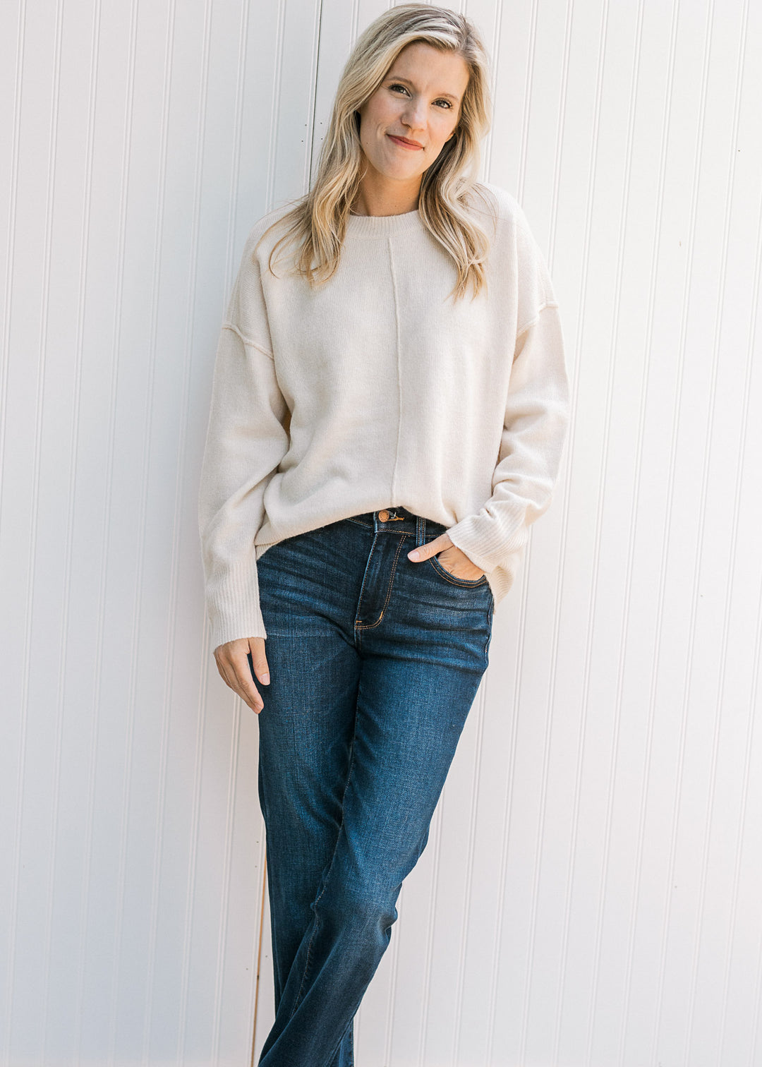 Model wearing jeans and a cream sweater with long sleeves, a round neck and seam down the front.