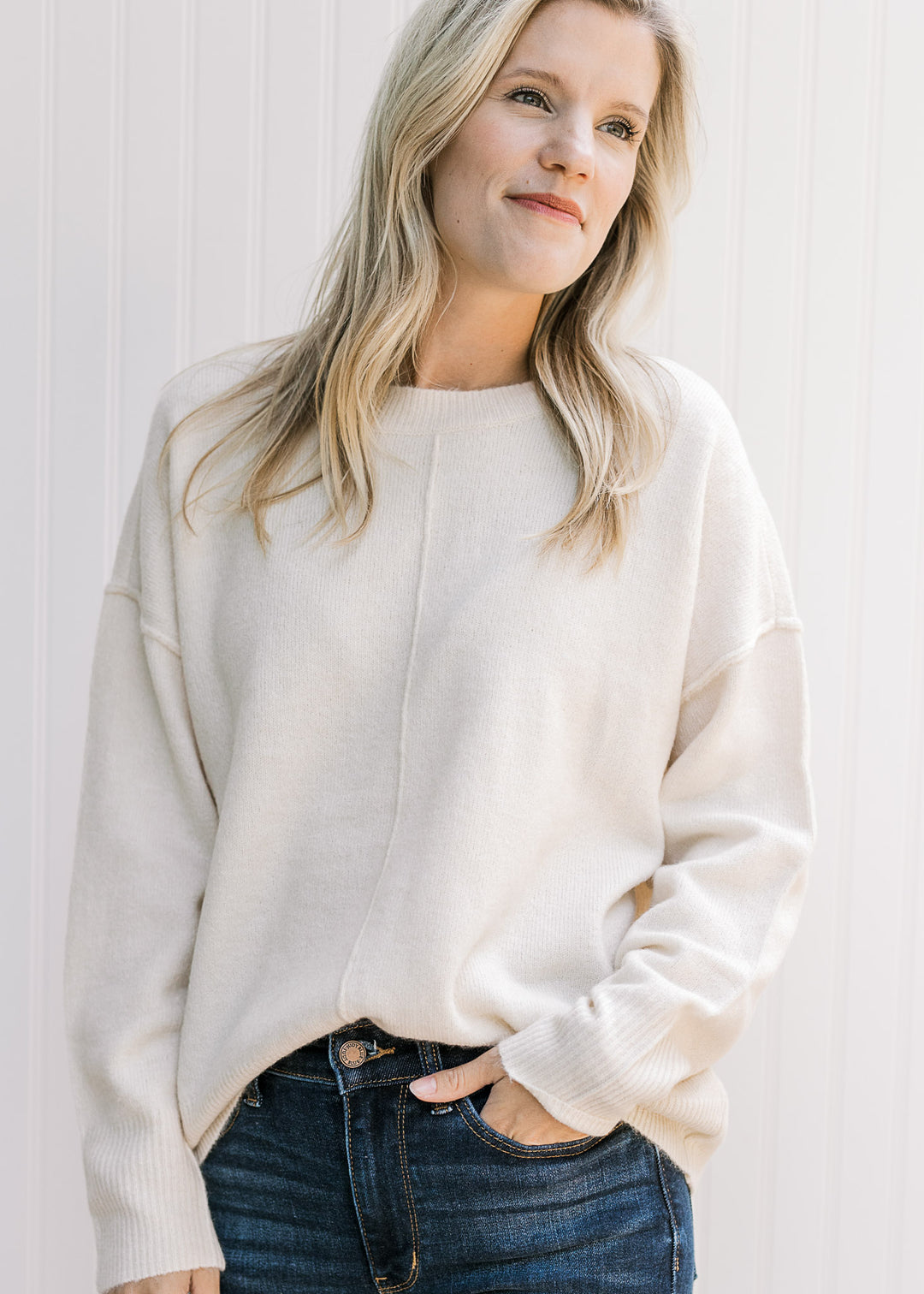 Model wearing a cream knit sweater with long sleeves, a round neck and seam down the front.